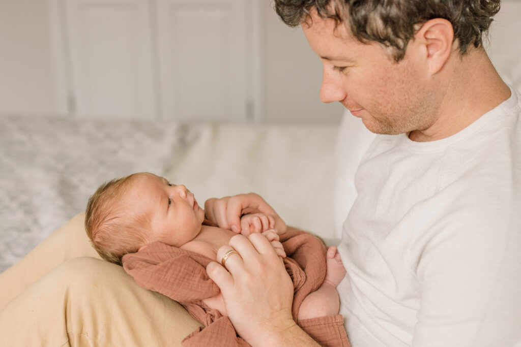 Dad looking at baby on bed |  Newborn Photos with Toddler with Janet Winter Photography