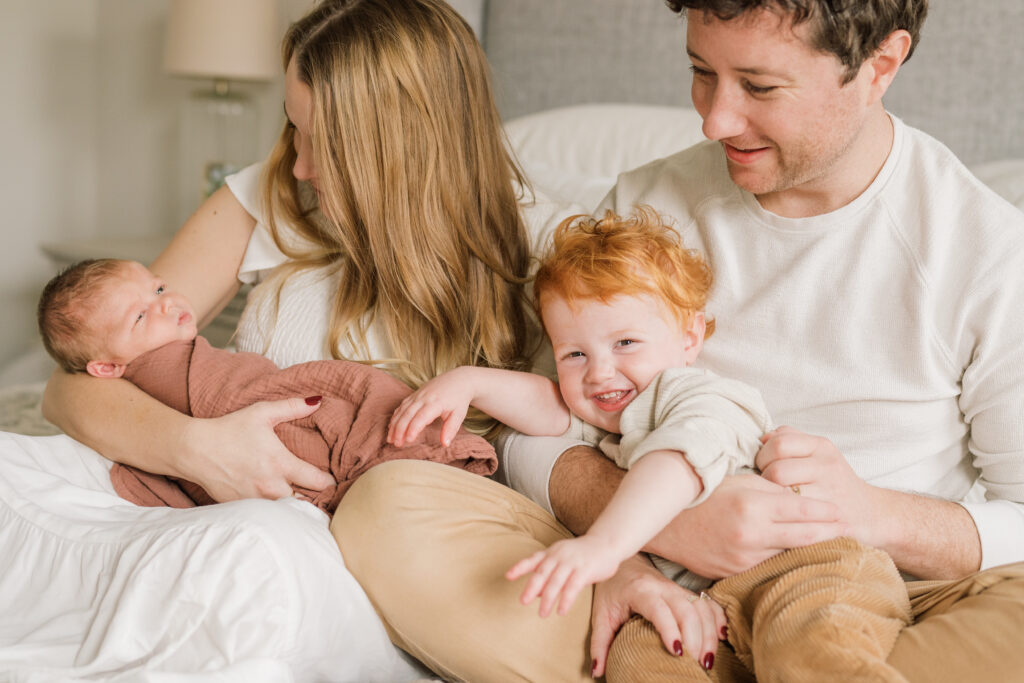 Family snuggling on bed with toddler and baby | Newborn Photos with Toddler with Janet Winter Photography