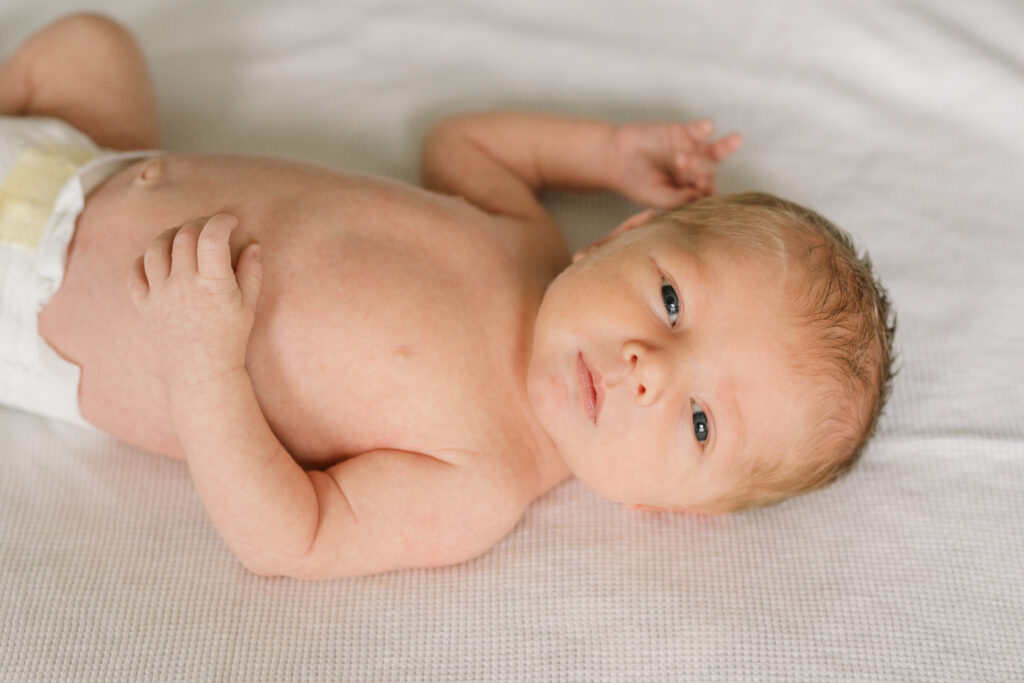 Baby boy laying on a cream blanket looking at the camera |  Newborn Photos with Toddler with Janet Winter Photography