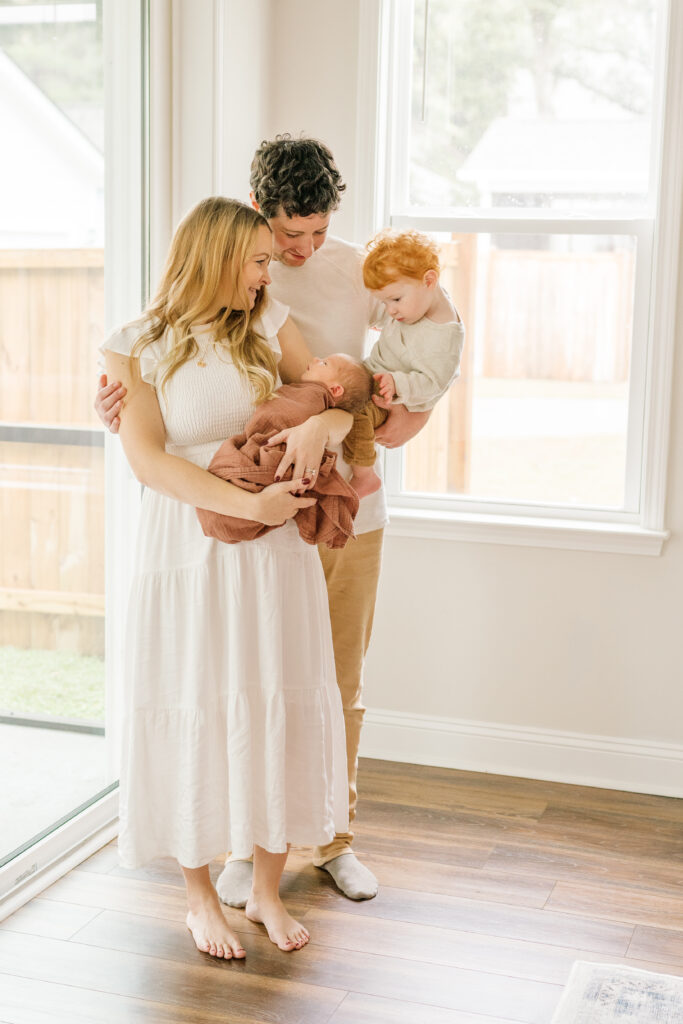 Family barefoot and in neutral colors enjoying a moment where toddler looks at new baby |  Newborn Photos with Toddler with Janet Winter Photography