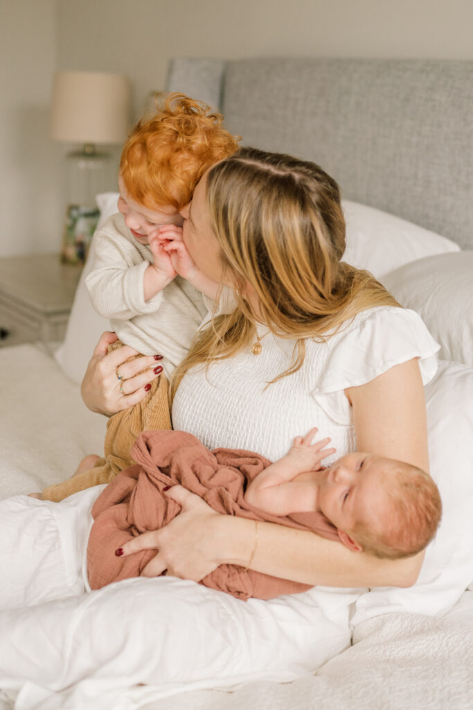 Mom enjoying a sweet moment with her toddler and baby on the bed during newborn session on johns island |  Newborn Photos with Toddler with Janet Winter Photography