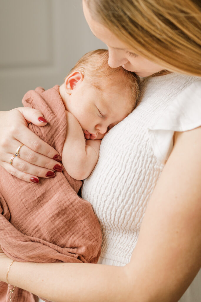 mom snuggling sweet baby on her chest while he is wrapped in a swaddle |  Newborn Photos with Toddler with Janet Winter Photography