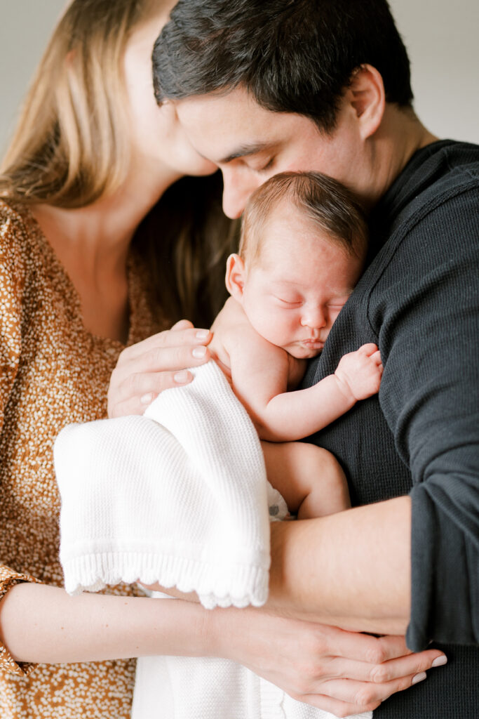 dad holds baby girl and mom gives a kiss - In-Home Newborn Photos - Johns Island Photographer